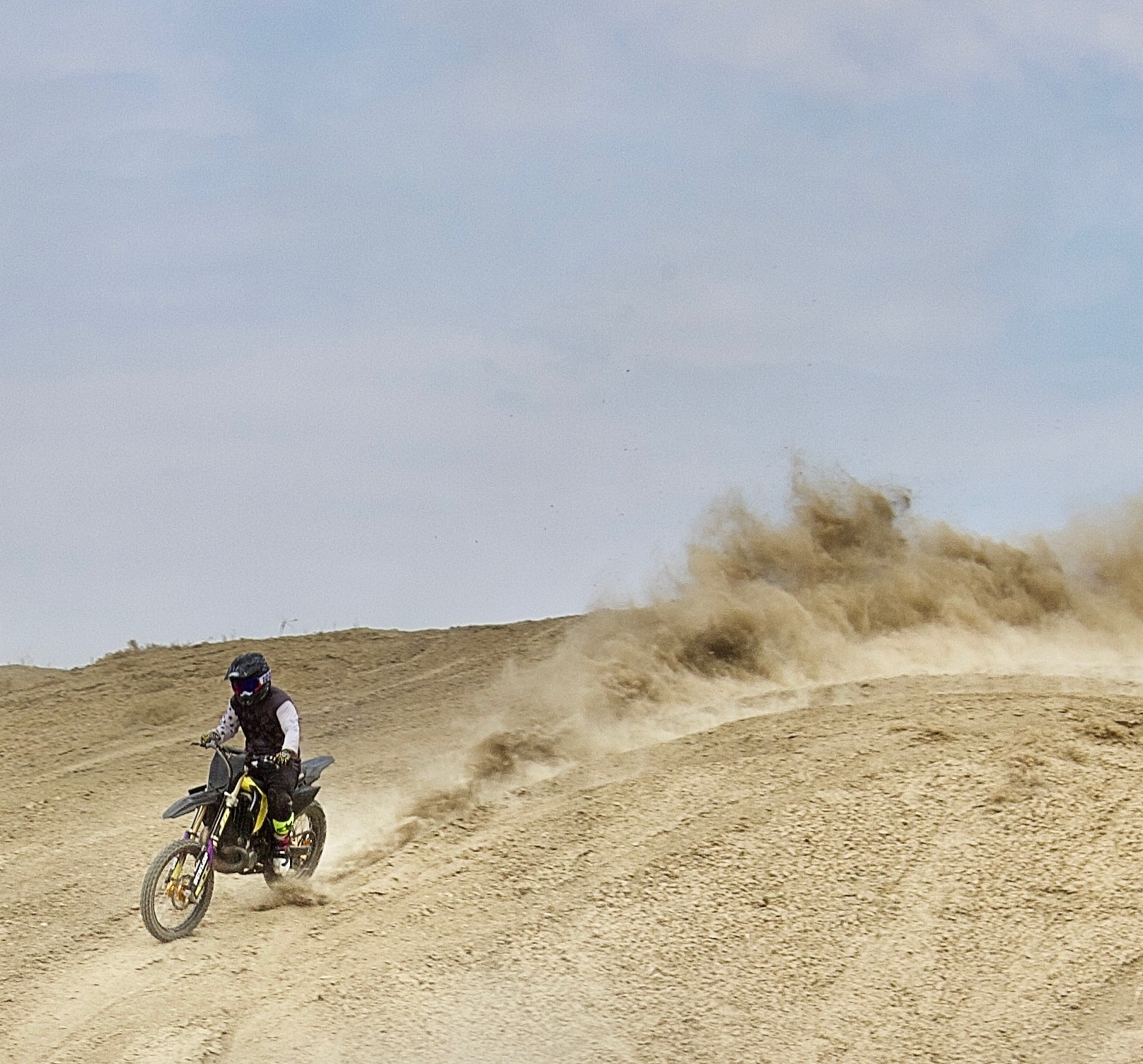 Dirt bike rider trailing dust over a hill