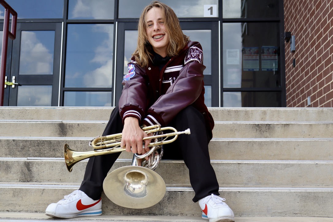 Senior seated on school steps holding a trumpet